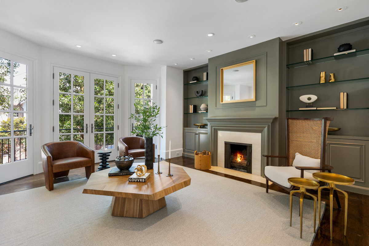 Living room with french doors to balcony, fireplace flanked by cabinetry