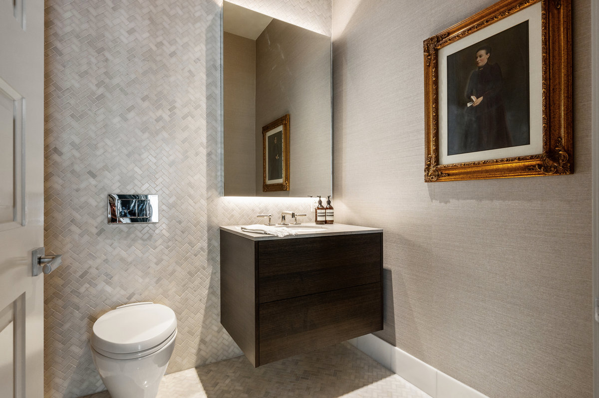 Powder room with herringbone marble tiles on one wall and floor, neutral grasscloth wall covering on remaining walls